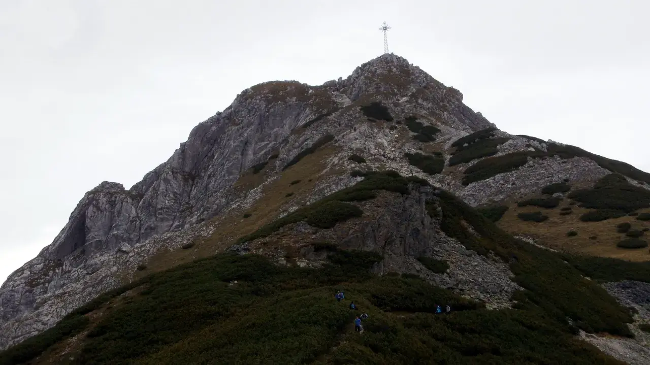 Grupa turystów wspina się na szczyt Giewontu, gdzie widoczny jest krzyż. Wjazd na Giewont to wyzwanie dla każdego miłośnika gór.