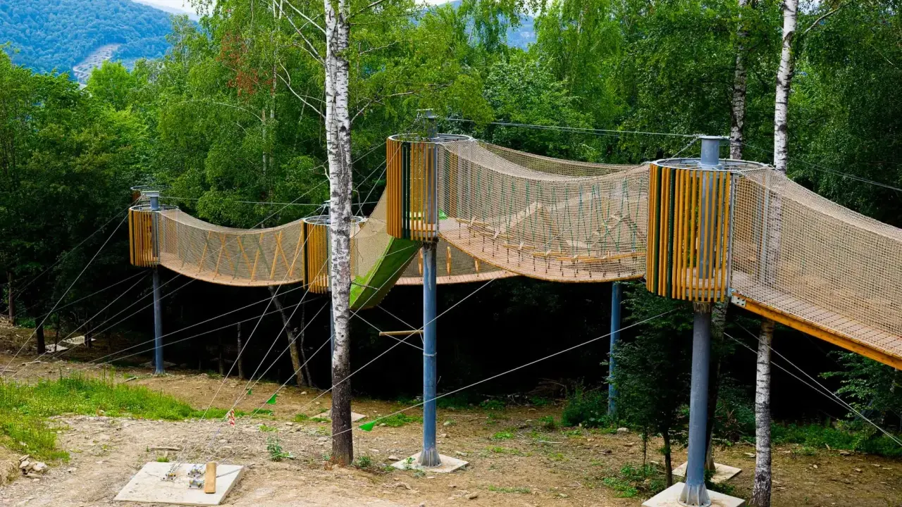 Drewniana, siatkowa kładka zawieszona między drzewami, idealna na przygodową solina plaża dla dzieci.