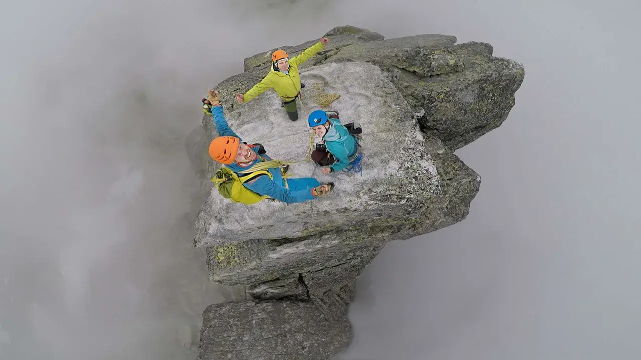 Trzech wspinaczy na szczycie Mnicha w Tatrach, otoczonych mgłą. Radość i adrenalina na twarzach.