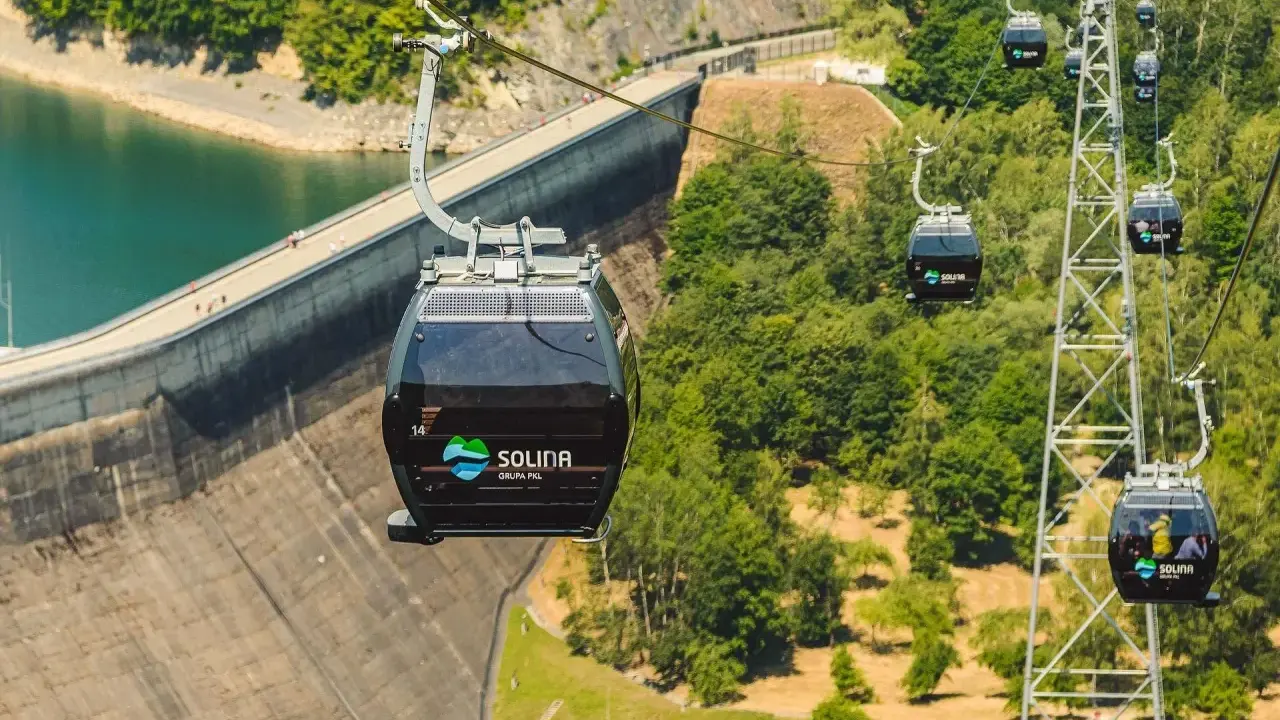 Kolejka linowa Solina z gondolami sunącymi nad zaporą i zielonymi wzgórzami.
