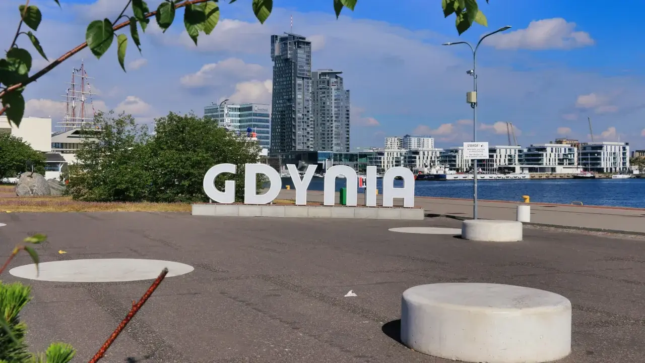 Napis GDYNIA na tle nowoczesnej architektury i żaglowca. Odkryj atrakcje Gdyni!