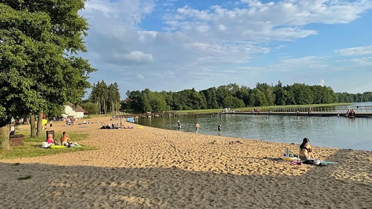 Słoneczna plaża w Insku z ludźmi odpoczywającymi na piasku i kąpiącymi się w jeziorze.