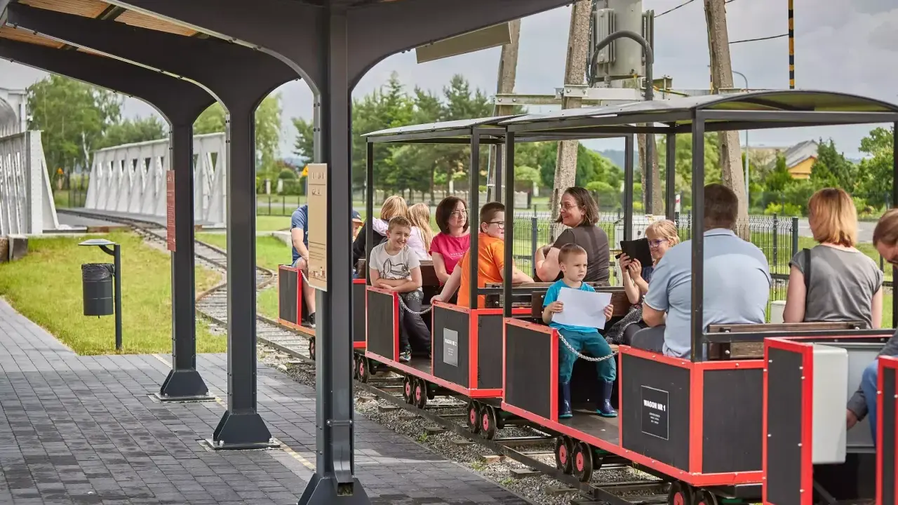 Wesołe **roztocze z dziećmi** podróżują kolejką wąskotorową. Uśmiechnięte twarze, letnia pogoda i zielone otoczenie tworzą radosną atmosferę.