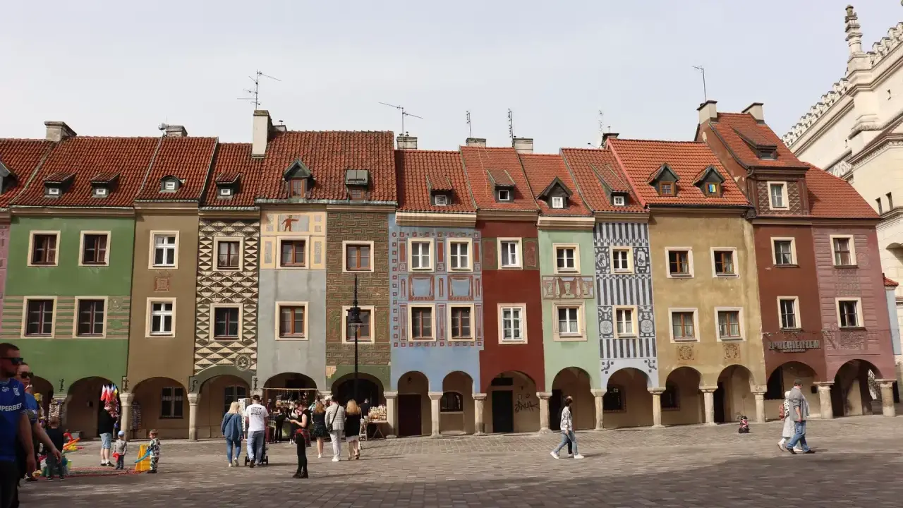 Kolorowe kamienice na Rynku w Poznaniu, sercu Polski. Ludzie spacerują po brukowanym placu.