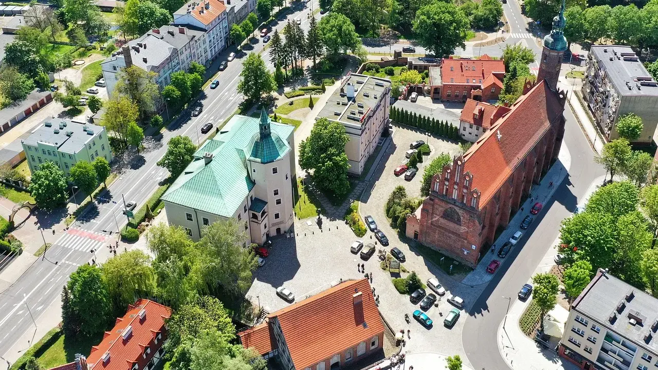 Słupsk atrakcje: zamek Książąt Pomorskich z zielonym dachem i ceglany kościół. W tle budynki mieszkalne i drzewa.