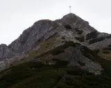 Grupa turystów wspina się na szczyt Giewontu, gdzie widoczny jest krzyż. Wjazd na Giewont to wyzwanie dla każdego miłośnika gór.