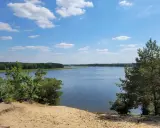 Piękny, spokojny dzień nad jeziorem Maziarnia. Błękitne niebo z białymi chmurkami, otoczone zielonym lasem.