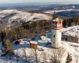 Wieża widokowa na Biskupiej Kopie w zimowej scenerii. Śnieg otula lasy i wzgórza, a budowle tworzą malowniczy krajobraz.