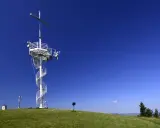 Wieża widokowa na górze Grzywackiej z krzyżem i spiralnymi schodami na tle błękitnego nieba.