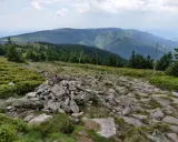 Kamienista ścieżka prowadzi przez zielone zbocza. W oddali widać pasmo górskie, które przypomina krajobraz z Lądka Zdroju.