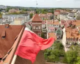 Widok na miasto z polską flagą na pierwszym planie. W tle widać zabytkowe kamienice i wieżę kościelną, co sugeruje ciekawe lidzbark warmiński atrakcje.