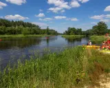 Spływ kajakowy w Załęczańskim Parku Krajobrazowym. Ludzie przygotowują się do wodnej przygody na piaszczystej plaży nad rzeką.