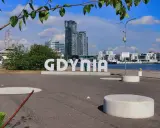 Napis GDYNIA na tle nowoczesnej architektury i żaglowca. Odkryj atrakcje Gdyni!