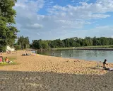 Słoneczna plaża w Insku z ludźmi odpoczywającymi na piasku i kąpiącymi się w jeziorze.