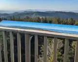 Widok z wieży widokowej na Beskid Sądecki. Na pierwszym planie drewniana balustrada, dalej panorama gór i lasów z tablicą informacyjną o szczytach.