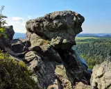 Wielkie, szare skały na szczycie góry, z których roztacza się widok na zielone lasy i pola.