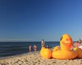 Słoneczna plaża w Bobolinie, dmuchana kaczka i inne atrakcje dla dzieci. Rodziny kąpią się w morzu.