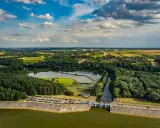 Malowniczy krajobraz z jeziorem Chańcza, zaporą, lasami i polami uprawnymi pod błękitnym, chmurowym niebem.