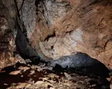 Wnętrze jaskini Mylnej, gdzie kamienne ściany i sufit tworzą mroczne, skaliste korytarze. W oddali widać ciemne przejście, a na ziemi leżą kamienie.
