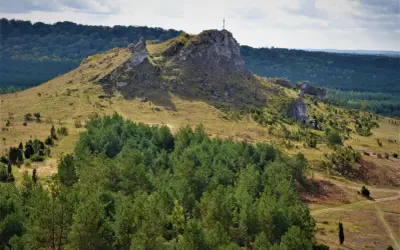 Góra Biakło z krzyżem na szczycie, otoczona lasami i skalistymi wzniesieniami.