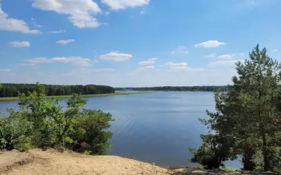 Piękny, spokojny dzień nad jeziorem Maziarnia. Błękitne niebo z białymi chmurkami, otoczone zielonym lasem.