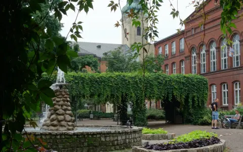 Fontanna i zielone arkady w parku miejskim, w tle zabytkowa architektura. Leszno atrakcje zachęcają do odpoczynku.