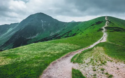 Kręta ścieżka wije się po zielonych zboczach gór. Wołowiec trasa zaprasza do wędrówki pod pochmurnym niebem.