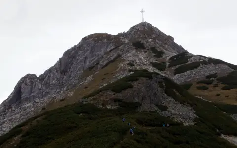 Grupa turystów wspina się na szczyt Giewontu, gdzie widoczny jest krzyż. Wjazd na Giewont to wyzwanie dla każdego miłośnika gór.