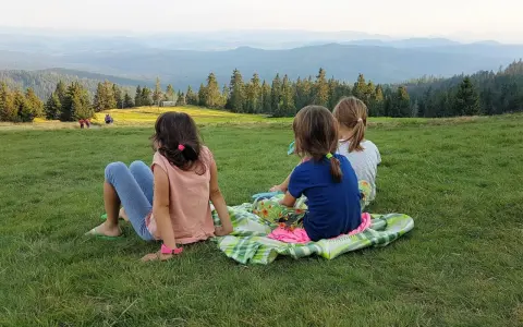 Trzy dziewczynki odpoczywają na kocu, podziwiając malowniczy widok gór i lasów. Może to właśnie szlak rysianka?