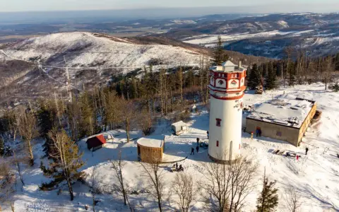 Wieża widokowa na Biskupiej Kopie w zimowej scenerii. Śnieg otula lasy i wzgórza, a budowle tworzą malowniczy krajobraz.