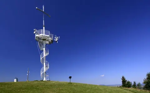 Wieża widokowa na górze Grzywackiej z krzyżem i spiralnymi schodami na tle błękitnego nieba.