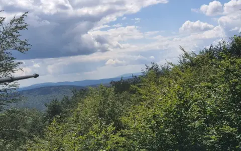Widok z Magury Wątkowskiej na zalesione wzgórza i niebo z chmurami.