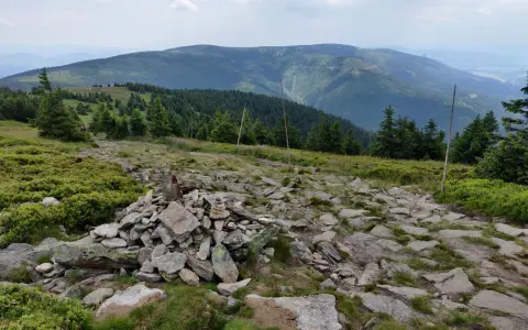 Kamienista ścieżka prowadzi przez zielone zbocza. W oddali widać pasmo górskie, które przypomina krajobraz z Lądka Zdroju.