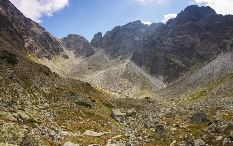 Kamienista dolina w Tatrach Wysokich, gdzie wije się szlak. W tle skaliste szczyty i błękitne niebo z chmurami.
