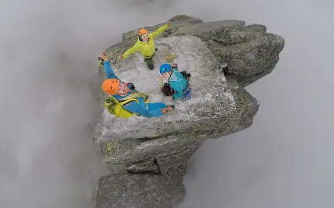 Trzech wspinaczy na szczycie Mnicha w Tatrach, otoczonych mgłą. Radość i adrenalina na twarzach.