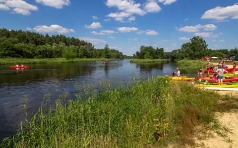 Spływ kajakowy w Załęczańskim Parku Krajobrazowym. Ludzie przygotowują się do wodnej przygody na piaszczystej plaży nad rzeką.