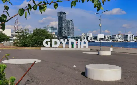 Napis GDYNIA na tle nowoczesnej architektury i żaglowca. Odkryj atrakcje Gdyni!