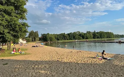 Słoneczna plaża w Insku z ludźmi odpoczywającymi na piasku i kąpiącymi się w jeziorze.