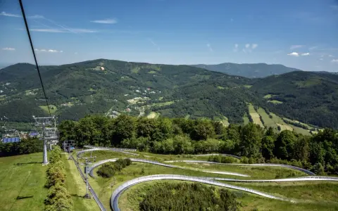 Tor saneczkowy na szlak na Czantorię z Ustronia, z widokiem na zielone wzgórza i niebo.