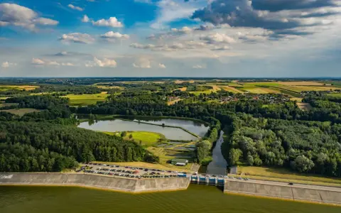 Malowniczy krajobraz z jeziorem Chańcza, zaporą, lasami i polami uprawnymi pod błękitnym, chmurowym niebem.