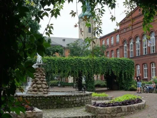 Fontanna i zielone arkady w parku miejskim, w tle zabytkowa architektura. Leszno atrakcje zachęcają do odpoczynku.
