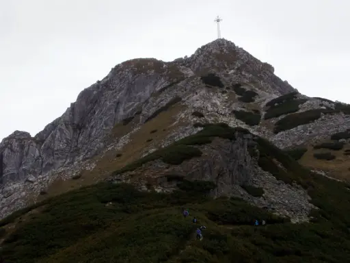 Grupa turystów wspina się na szczyt Giewontu, gdzie widoczny jest krzyż. Wjazd na Giewont to wyzwanie dla każdego miłośnika gór.