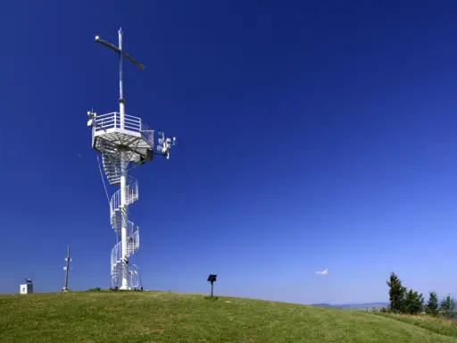Wieża widokowa na górze Grzywackiej z krzyżem i spiralnymi schodami na tle błękitnego nieba.