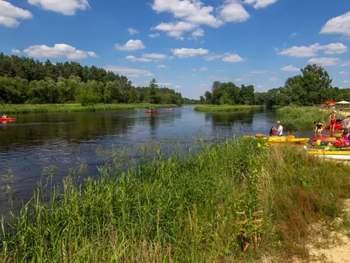 Spływ kajakowy w Załęczańskim Parku Krajobrazowym. Ludzie przygotowują się do wodnej przygody na piaszczystej plaży nad rzeką.