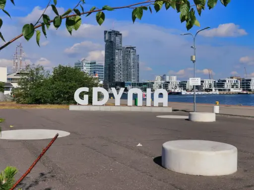 Napis GDYNIA na tle nowoczesnej architektury i żaglowca. Odkryj atrakcje Gdyni!