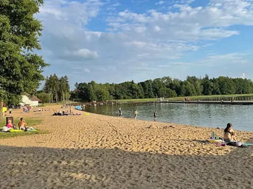 Słoneczna plaża w Insku z ludźmi odpoczywającymi na piasku i kąpiącymi się w jeziorze.