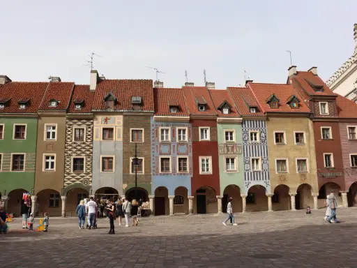 Kolorowe kamienice na Rynku w Poznaniu, sercu Polski. Ludzie spacerują po brukowanym placu.