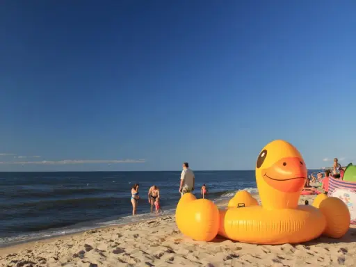 Słoneczna plaża w Bobolinie, dmuchana kaczka i inne atrakcje dla dzieci. Rodziny kąpią się w morzu.