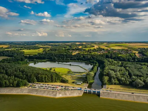 Malowniczy krajobraz z jeziorem Chańcza, zaporą, lasami i polami uprawnymi pod błękitnym, chmurowym niebem.