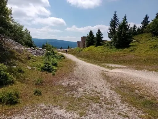 Droga na Wysoką Kopę. Kręty szlak prowadzi przez zielone wzgórza, w oddali widać budynek i góry.